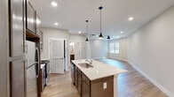 This single-story unit located along Alt US-72 W in Huntsville, Alabama, offers a thoughtfully designed open-concept layout with contemporary finishes throughout. The kitchen serves as the centerpiece of the living area, featuring rich, dark-toned cabinetry with brushed nickel hardware, light quartz countertops, a stainless steel appliance suite including a refrigerator, range, and over-the-range microwave, and a peninsula with an undermount sink. Stylish pendant lights hang above the peninsula, complementing the recessed lighting overhead. The adjoining living area is finished with wood-look plank flooring and includes a ceiling fan, with a window allowing natural light to fill the space.

The bedrooms are carpeted for comfort, each equipped with a ceiling fan and a window with blinds. One bedroom connects to a generously sized walk-in closet outfitted with wire shelving on multiple walls. Two bathrooms mirror each other in design, featuring wood-toned vanities with quartz counters, undermount sinks, and wood-look flooring. One includes a shower-tub combination. The overall aesthetic is clean and neutral, creating a bright, move-in-ready environment.