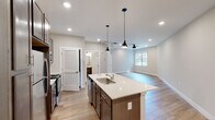 This single-story unit located along Alt US-72 W in Huntsville, Alabama, offers a thoughtfully designed open-concept layout with contemporary finishes throughout. The kitchen serves as the centerpiece of the living area, featuring rich, dark-toned cabinetry with brushed nickel hardware, light quartz countertops, a stainless steel appliance suite including a refrigerator, range, and over-the-range microwave, and a peninsula with an undermount sink. Stylish pendant lights hang above the peninsula, complementing the recessed lighting overhead. The adjoining living area is finished with wood-look plank flooring and includes a ceiling fan, with a window allowing natural light to fill the space.

The bedrooms are carpeted for comfort, each equipped with a ceiling fan and a window with blinds. One bedroom connects to a generously sized walk-in closet outfitted with wire shelving on multiple walls. Two bathrooms mirror each other in design, featuring wood-toned vanities with quartz counters, undermount sinks, and wood-look flooring. One includes a shower-tub combination. The overall aesthetic is clean and neutral, creating a bright, move-in-ready environment.