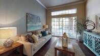 This single-floor residence is thoughtfully designed with a functional and cohesive layout. The living room serves as a central gathering space, featuring rich hardwood-style flooring, elevated ceilings with crown molding, and a large sliding glass door topped with transom windows that flood the room with natural light and provide views of the landscaped exterior. A dedicated dining area accommodates a glass-top table and upholstered chairs, with a pass-through opening connecting conveniently to the kitchen. The kitchen is outfitted with ample white cabinetry, generous counter space, and white appliances, with direct access to the in-unit laundry room, which includes a full-size washer and dryer alongside built-in wire shelving for storage. A versatile room features built-in shelving, a fireplace with a white surround, and a window for natural light, making it well-suited as an office or flex space. The bedroom includes carpet flooring, a fireplace, and a window allowing natural light. The bathroom offers a tub-shower combination, a single-sink vanity, and an adjacent walk-in closet with wire shelving. Throughout the home, crown molding, hardwood-style flooring, and neutral tones contribute to a polished, cohesive aesthetic.