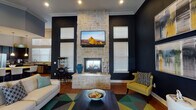 Located at 5702 Timbergate Dr in Corpus Christi, Texas, this single-floor amenity space delivers a bold and sophisticated interior designed for both relaxation and gathering. The centerpiece of the main lounge is a striking floor-to-ceiling natural stone fireplace flanked by a wall-mounted TV, set against deep navy blue walls that create a dramatic, upscale atmosphere. Soaring ceilings with crown molding add a sense of grandeur, while warm hardwood flooring flows throughout. Seating areas are accented with mustard yellow accent chairs, geometric-patterned area rugs in teal, yellow, and grey, and contemporary abstract artwork that ties the color palette together cohesively.

The space transitions into a casual dining and lounge area featuring high-top tables with upholstered chairs, additional wall art, and a secondary wall-mounted TV — ideal for informal meetings or social gatherings. A dedicated conference room offers a rustic wood table surrounded by plush grey chairs beneath tall, light-filled windows, providing a professional yet comfortable setting.

The kitchen is outfitted with dark cabinetry, granite countertops, stainless steel appliances including a refrigerator, dishwasher, and microwave, complemented by ample natural light from a multi-pane window. Every area of this space reflects a cohesive, modern design aesthetic.