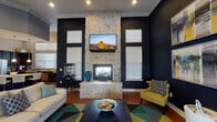Located at 5702 Timbergate Dr in Corpus Christi, Texas, this single-floor amenity space delivers a bold and sophisticated interior designed for both relaxation and gathering. The centerpiece of the main lounge is a striking floor-to-ceiling natural stone fireplace flanked by a wall-mounted TV, set against deep navy blue walls that create a dramatic, upscale atmosphere. Soaring ceilings with crown molding add a sense of grandeur, while warm hardwood flooring flows throughout. Seating areas are accented with mustard yellow accent chairs, geometric-patterned area rugs in teal, yellow, and grey, and contemporary abstract artwork that ties the color palette together cohesively.

The space transitions into a casual dining and lounge area featuring high-top tables with upholstered chairs, additional wall art, and a secondary wall-mounted TV — ideal for informal meetings or social gatherings. A dedicated conference room offers a rustic wood table surrounded by plush grey chairs beneath tall, light-filled windows, providing a professional yet comfortable setting.

The kitchen is outfitted with dark cabinetry, granite countertops, stainless steel appliances including a refrigerator, dishwasher, and microwave, complemented by ample natural light from a multi-pane window. Every area of this space reflects a cohesive, modern design aesthetic.