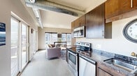 Located at 101 Summit St in Duluth, Minnesota, this thoughtfully designed studio unit offers an efficient, open-concept layout that makes excellent use of its compact footprint. The space blends modern industrial aesthetics with functional living, highlighted by exposed metallic ductwork running along the ceiling — a defining architectural detail that adds urban character throughout.

The kitchen is well-appointed with rich, dark-stained cabinetry, granite-style countertops, and a full suite of stainless steel appliances including a range, over-the-range microwave, dishwasher, and full-size refrigerator. Ample upper and lower cabinet storage ensures practicality without compromising style.

The open living area flows seamlessly from the kitchen, bathed in natural light from large, multi-pane windows that frame views of the surrounding Duluth skyline and neighboring architecture. Sliding glass doors lead to an expansive shared outdoor terrace, furnished with seating and dining areas — an ideal extension of the interior living space.

Neutral wall tones, recessed lighting, and a warm color palette create a welcoming and versatile ambiance. The unit's single-floor layout ensures ease of movement, while its position within the building provides elevated outdoor views. This space is ideal for those seeking modern, low-maintenance urban living in the heart of Duluth.