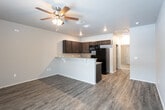 Located in Lubbock, TX, this single-floor home offers a well-designed, open-concept layout that seamlessly connects the kitchen and living areas. The kitchen is outfitted with rich, dark espresso cabinetry featuring sleek hardware, granite-style countertops, a full suite of black appliances including a refrigerator, range, and microwave, and a stainless steel sink. A raised breakfast bar with corbel accents provides a natural divide between the kitchen and the adjoining living space, which is finished with durable gray-toned vinyl plank flooring and a ceiling fan overhead. Recessed lighting throughout the kitchen and living areas ensures a bright, welcoming ambiance. A dedicated bedroom area is finished with plush carpeting and benefits from a window that allows natural light to fill the room, accompanied by a paneled entry door. The bathroom is appointed with matching dark cabinetry, a granite-style vanity countertop, vinyl plank flooring, and a full bathtub and shower combination. Neutral gray walls throughout the home provide a clean, cohesive aesthetic that complements the dark wood tones of the cabinetry and the warm flooring, creating a practical and comfortable living environment.