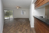 This well-appointed 2-bedroom, 2-bathroom single-floor residence offers a comfortable and functional layout throughout. Rich, dark hardwood-style flooring runs consistently through the living areas, bedrooms, and hallways, creating a cohesive and warm aesthetic. Ceiling fans with integrated light fixtures are present in the main living area and both bedrooms, providing both comfort and illumination.

The living room is generously sized, featuring vertical blind window treatments and a sliding glass door that opens to an outdoor area, allowing natural light to fill the space. A standout feature is the kitchen's rustic wood-clad breakfast bar with a dark granite-style countertop that opens to the living area, creating an inviting pass-through design. The kitchen is equipped with black appliances, white cabinetry, and matching dark countertops, with access to a dedicated laundry area.

Both bedrooms offer ample space, vertical blinds, and ceiling fans. One bedroom includes two bifold closets, providing excellent storage. Each bathroom features a white vanity with dark countertops, a lighted mirror, and a shower/tub combination. Textured ceilings are found throughout, and clean white walls and trim complete the bright, neutral interior palette.
