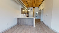 Located at 165 Thorndike, this single-floor unit showcases a striking blend of industrial and contemporary design elements throughout. The open-concept living and kitchen area immediately draws the eye upward to the warm wood-plank ceiling, accented by exposed metal ductwork, track lighting, and original timber support columns — details that lend the space an authentic loft-like character.

The kitchen is well-appointed with wood-grain cabinetry extending to the ceiling, a textured white tile backsplash, and a full suite of stainless steel appliances including a refrigerator, range, and over-the-range microwave. A large island with a white quartz countertop and wood-paneled base provides additional prep space and casual seating. Pendant lighting overhead reinforces the modern industrial aesthetic. A stacked washer and dryer unit is conveniently integrated near the kitchen.

The living area is bright and airy, with light wood-tone flooring, clean white walls, and elevated ceilings that contribute to a spacious, open feel. Doors lead to private rooms, offering comfortable separation from the main living space.

The bathroom is finished to a high standard, featuring large-format marble-look tile on both the walls and floor, a soaking tub with a frameless glass sliding shower enclosure, a floating wood vanity with white quartz countertop, and modern brushed chrome fixtures throughout.