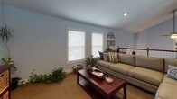 Located at 5820 Murray Dr in Hanahan, South Carolina, this two-story facility is thoughtfully designed to serve as a multifunctional community or recreational space. The upper level features an open-concept layout with soft blue walls, plush carpeting, and generous natural light streaming through multiple windows. A curved bar-style kitchenette anchors one area of the floor, complete with upper cabinetry, a refrigerator, microwave, wall-mounted television, and bar seating for several guests — ideal for casual gatherings or events. Adjacent to the kitchenette, a spacious dining area with dark wood chairs and a long table offers a comfortable setting for group meals or meetings. A cozy lounge area with a sectional sofa, coffee table, and accent décor provides a relaxed retreat, while a dedicated display area with wall shelving and framed artwork adds a personalized touch. A grand staircase with white balusters connects the two levels, creating a welcoming transition between floors. The lower level houses a well-appointed fitness center featuring bold blue walls with decorative accent graphics, rubber flooring, full-length mirrors, and a wide array of cardio and strength equipment including ellipticals, treadmills, rowing machines, and a cable machine. Together, the two floors create a versatile space well-suited for both active wellness and social community engagement.