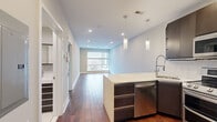 This well-appointed one-bedroom, one-bathroom unit offers a thoughtfully designed open-concept layout that maximizes its efficient footprint. Rich hardwood flooring runs throughout the main living areas, complementing the neutral gray tones of the walls and creating a warm, modern aesthetic.

The kitchen is a standout feature, equipped with full stainless steel appliances including a double-oven range, built-in microwave, and French door refrigerator. Dark espresso cabinetry extends to the ceiling for ample storage, while a quartz-topped peninsula with pendant lighting provides both workspace and casual dining space, flowing naturally into the living area.

The living room benefits from oversized windows that frame urban views and fill the space with natural light. The bedroom includes a ceiling fan, access to additional window views, and a well-organized built-in closet with shelving.

The bathroom features large-format white tile flooring, a frameless glass sliding shower enclosure with dark stone-effect tile surround, a floating vanity with an integrated sink, and recessed lighting.

A dedicated laundry area accommodates a full-size stacked washer and dryer behind louvered doors, adding practical convenience to this compact yet complete urban residence.