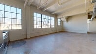 Located in the heart of Los Angeles's vibrant Arts District, this single-floor industrial loft at 445 S San Pedro St blends raw architectural character with modern finishes. The open-plan layout is defined by soaring ceilings with exposed wood beams, visible ductwork and piping, and polished concrete floors throughout, all lending an authentic loft aesthetic.

Oversized steel-framed factory windows dominate multiple walls, flooding the interior with abundant natural light and framing striking panoramic views of the Downtown Los Angeles skyline. Corner windows in particular create a dramatic, light-filled environment with sightlines extending across the city.

The kitchen is thoughtfully appointed with wood-toned cabinetry, dark countertops, stainless steel appliances including a refrigerator, range, microwave, and dishwasher, and a tile backsplash. It flows seamlessly into the expansive open living area, making the space well-suited for both everyday living and entertaining.

The bathroom features a glass-enclosed shower, a wood-grain vanity with a dark countertop and integrated sink, and a steel-framed window that continues the industrial design language found throughout the space. The overall ambiance is one of urban sophistication, combining the character of a historic industrial building with contemporary updates.
