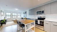 Located at West Westfield Avenue in Roselle Park, NJ, this thoughtfully designed one-bedroom, one-bathroom residence offers a cohesive, modern aesthetic throughout its efficiently arranged single-floor layout. Light wood flooring flows continuously through each room, anchoring the clean, neutral color palette that defines the space.

The open-concept kitchen and living area form the heart of the unit. The kitchen is outfitted with flat-front gray cabinetry extending to the ceiling, stainless steel appliances including a range, microwave, and dishwasher, and a crisp white quartz countertop complemented by a distinctive hexagonal tile backsplash. A freestanding dining table with bar seating bridges the kitchen and living area seamlessly.

The living room benefits from a generous bank of windows that frame views of the surrounding Roselle Park streetscape, flooding the space with natural light. The bedroom offers a comfortable footprint, a closet, and its own window with town views. The bathroom features floor-to-ceiling tile and a glass-enclosed shower. A hallway connects all rooms, contributing to the unit's efficient and practical flow.
