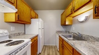 This one-bedroom, one-bathroom unit in Royal Oak, Michigan offers a functional single-floor layout designed to maximize the use of its compact footprint. The galley-style kitchen is outfitted with warm oak cabinetry extending to the ceiling on both sides, providing ample storage. Granite-patterned laminate countertops line both walls, accompanied by a stainless steel sink, a white electric range, refrigerator, and dishwasher. Wood-look vinyl plank flooring runs throughout the kitchen, lending a clean, durable surface.

The living area is carpeted in neutral grey and features baseboard heating along the exterior wall, with large windows that invite natural light and views of the surrounding neighborhood. Built-in open shelving and a louvered closet offer convenient storage directly within the living space.

The bedroom is similarly carpeted and bathed in natural light through a window fitted with white blinds. Baseboard heating is present here as well, ensuring consistent comfort throughout.

The bathroom includes a white tile floor, a full tub and shower combination with white square-tile surround and grab bar, an oak vanity, and granite-patterned countertop. The overall palette of the unit is neutral and light, creating a clean, move-in-ready atmosphere.