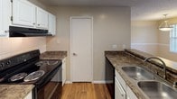 Located at 7914 University Ridge Dr in Charlotte, NC, this single-floor residence offers a well-organized layout designed for comfortable everyday living. The kitchen is appointed with white cabinetry, dark granite-style countertops, hardwood flooring, a black refrigerator, electric range, and a dishwasher — all arranged in a galley-style configuration that maximizes efficiency. A peninsula with a stainless steel sink provides additional prep space and opens toward the main living area. The combined living and dining space is generously sized, featuring plush carpeting, textured ceilings, and multiple windows that invite natural light from multiple angles. Pendant and ceiling-mounted light fixtures provide warm illumination throughout. A dedicated dining area is defined by a hanging pendant light, while the adjacent living space benefits from a ceiling fan fixture. The bedroom is carpeted and features a window with outdoor views, offering a quiet and comfortable retreat. The bathroom is finished with hardwood flooring, white cabinetry, a wide vanity mirror with overhead lighting, dark countertops, and a tub-shower combination with tiled surround. Throughout the residence, neutral warm tones create a cohesive and inviting atmosphere.
