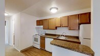 This single-floor residence offers a practical and comfortable layout with two bedrooms and one and a half bathrooms. The kitchen is a standout feature, showcasing warm honey-toned wood cabinetry that provides ample storage space. Dark granite-look countertops add a touch of character and contrast against the white appliances, which include an electric range, dishwasher, and a stainless steel sink. Light wood-style flooring runs throughout the kitchen, contributing to a bright and cohesive aesthetic. The neutral white walls and flush-mount ceiling light keep the space feeling clean and well-lit. The kitchen's layout is designed for efficiency, with countertop space extending along two walls to maximize workspace. The overall design of the home strikes a balance between functionality and comfort, making it a solid choice for those seeking a straightforward, move-in-ready living space. The single-floor plan ensures easy accessibility throughout, while the thoughtful use of materials and finishes gives the home a tidy, well-maintained appearance.