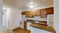 This single-floor residence offers a practical and comfortable layout with two bedrooms and one and a half bathrooms. The kitchen is a standout feature, showcasing warm honey-toned wood cabinetry that provides ample storage space. Dark granite-look countertops add a touch of character and contrast against the white appliances, which include an electric range, dishwasher, and a stainless steel sink. Light wood-style flooring runs throughout the kitchen, contributing to a bright and cohesive aesthetic. The neutral white walls and flush-mount ceiling light keep the space feeling clean and well-lit. The kitchen's layout is designed for efficiency, with countertop space extending along two walls to maximize workspace. The overall design of the home strikes a balance between functionality and comfort, making it a solid choice for those seeking a straightforward, move-in-ready living space. The single-floor plan ensures easy accessibility throughout, while the thoughtful use of materials and finishes gives the home a tidy, well-maintained appearance.