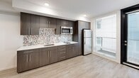 Located in the Ballard neighborhood of Seattle, WA, this modern studio unit at 5512 17th Ave NW offers a thoughtfully designed layout that maximizes every inch of its compact footprint. The single-floor plan encompasses an open-concept kitchen and living area, a full bathroom, and a private patio.

The kitchen is a standout feature, outfitted with rich dark-wood cabinetry, a vibrant multicolor mosaic tile backsplash, white countertops, and a full suite of stainless steel appliances including a refrigerator, microwave, and cooktop. Large windows flood the kitchen and living area with natural light and provide views of the patio, enhancing the sense of openness. Light wood-tone luxury vinyl plank flooring runs throughout the main living space, complementing the contemporary aesthetic.

The bathroom continues the modern design language with matching dark-wood vanity cabinetry, a white undermount sink, large-format tile flooring, and the same eye-catching mosaic tile accents found in the kitchen. A combined tub and shower completes the space.

A sleek, dark panel door with brushed chrome hardware serves as a striking architectural accent at the entry. The patio provides an outdoor retreat, extending the livable space beyond the interior. Recessed lighting throughout keeps the unit bright and polished.