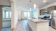 This single-floor residence features a thoughtfully designed open-concept layout that seamlessly connects the kitchen and living areas. The kitchen is a standout space, anchored by a large central island topped with speckled granite countertops and equipped with a stainless steel undermount sink and brushed nickel faucet. Taupe shaker-style cabinetry pairs with a white subway tile backsplash, while stainless steel appliances — including a refrigerator, range, and microwave — complete the modern aesthetic. Light wood-look flooring extends throughout the main living area, complemented by a combination of recessed lighting, pendant lights over the island, and a chandelier that adds a refined touch near the dining space. Natural light flows in through large windows, offering open outdoor views. The bedrooms are finished with plush carpet and ceiling fans, providing a comfortable retreat. One bedroom benefits from dual windows with scenic views. A full bathroom features a granite-topped vanity with gray cabinetry, tile-surround soaking tub, and wood-look tile flooring. A generously sized walk-in closet with dual hanging rods and built-in shelving adds practical storage.