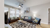 This well-appointed single-floor residence offers a thoughtfully designed layout that balances comfort and modern style. The living room serves as the heart of the home, featuring light-toned walls, wood-look flooring, a ceiling fan, and generous windows dressed with blinds and curtains that invite abundant natural light. Multiple seating areas are anchored by a bold geometric area rug, creating a warm and inviting atmosphere.

The kitchen is a standout feature, showcasing rich wood-grain cabinetry, crisp white quartz countertops, and a full suite of stainless steel appliances including a refrigerator, range, microwave, and dishwasher. A spacious island with bar seating and pendant lighting adds both function and elegance, while wood-look flooring ties the space together seamlessly.

Each bedroom offers a cozy, functional retreat with carpeted floors, windows with natural light, and ample room for furnishings. One bedroom includes direct access to a walk-in closet adjacent to a vanity area with wood cabinetry and a white countertop.

The bathrooms are finished with wood-toned cabinetry, white countertops, large mirrors, and combination tub-shower units, maintaining a clean and contemporary aesthetic consistent throughout the residence. The overall design reflects a cohesive modern sensibility with warm, neutral tones.