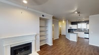 Located in Dallas, this single-floor residence offers a thoughtfully designed layout that blends comfort and functionality. The open living area serves as the heart of the home, anchored by a classic white-mantled fireplace that adds warmth and character. Adjacent to the fireplace, built-in shelving provides both display and storage space, framed by clean crown molding that carries throughout the space. Rich, dark hardwood-style flooring extends across the living area, creating a cohesive and inviting atmosphere. The kitchen is positioned in clear view of the living space, featuring white cabinetry, granite countertops, a stainless steel range, and a striking dark subway tile backsplash that adds a modern contrast. Recessed lighting and pendant fixtures illuminate the space effectively, complementing the neutral gray-toned walls that lend a contemporary, versatile aesthetic. A hallway visible from the main living area leads to additional rooms, suggesting a practical and well-organized floor plan. Crown molding details and consistent finishes throughout reflect a refined attention to design. This Dallas residence combines classic architectural touches with modern updates, resulting in a space that is both stylish and highly livable.