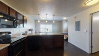 This single-floor unit offers an open, functional layout that seamlessly connects the kitchen, living, and sleeping areas. The kitchen is a standout feature, anchored by a large central island with a built-in sink and granite countertops that provide generous prep and dining space. Rich dark-stained cabinetry lines the walls, accented by glass-front upper cabinets and a full suite of black appliances, including a refrigerator, electric range, microwave, and dishwasher. Pendant lighting above the island adds warmth and visual interest, complementing the dark hardwood-style flooring that flows throughout the entire unit.

The open sleeping area is generously proportioned, featuring a wide window that brings in natural light and views of the surrounding landscape. A walk-in closet provides ample storage just off the bedroom space. The bathroom is well-appointed with a dark wood vanity, granite countertop, and a full tub-shower combination set against warm taupe-toned walls. Throughout the unit, a textured ceiling, flush-mount lighting, and clean white walls create a cohesive, neutral palette. The overall ambiance is modern and practical, offering a comfortable and well-designed living environment.