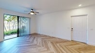 This thoughtfully designed one-bedroom, one-bathroom apartment in Royal Palm Beach, Florida, offers a seamless blend of modern aesthetics and functional living. Throughout the unit, striking herringbone-patterned hardwood floors create a visually dynamic foundation that unifies every room.

The open-concept kitchen and living area serves as the heart of the home. The kitchen is outfitted with stainless steel appliances, a combination of white upper cabinetry and warm natural wood lower cabinets, and a sleek white quartz peninsula with an integrated sink. Globe pendant lights with brass accents hang overhead, adding a contemporary, upscale touch.

The living area is bright and airy, featuring a ceiling fan, clean white walls, and a sliding glass door that opens directly to a lush outdoor garden space with mature palm trees — ideal for enjoying the Florida lifestyle.

The bedroom is a comfortable retreat with its own ceiling fan, a window framing peaceful water views of a neighboring lake, and continued herringbone flooring throughout.

The bathroom features a wood-toned vanity with a white countertop, full tub and shower combination with light neutral tile surround, and coordinating herringbone flooring. A hallway and dedicated closet complete this well-appointed home.