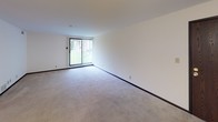 Located at 4718 N 100th St in Wauwatosa, Wisconsin, this single-floor unit offers a practical and comfortable layout designed for everyday living. The open living area is finished with neutral wall-to-wall carpeting and crisp white walls, creating a clean, bright atmosphere. A large sliding glass door fitted with vertical blinds fills the space with natural light while providing access to an outdoor view of lush greenery. The layout flows into a separate dining or secondary living area, also carpeted and illuminated by a pendant light fixture, with a dark-stained closet providing additional storage. The kitchen features dark wood cabinetry paired with light laminate countertops, a gas range, and a stainless steel sink, all set over hardwood-style flooring. Ample upper and lower cabinet storage makes this a highly functional cooking space. The bedroom is generously sized with carpeted flooring, a large window with vertical blinds allowing in natural light, and a spacious walk-in closet with built-in shelving and a hanging rod. The full bathroom is outfitted with white tile flooring, a vanity with integrated sink and storage cabinetry, a toilet, and a full tub-shower combination accented with classic tan wall tile, offering a clean and functional design throughout.