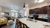 This single-story residence showcases a thoughtfully designed open-concept layout that seamlessly connects the kitchen, dining, and living areas. The kitchen is a standout feature, equipped with rich dark-wood cabinetry, granite countertops with a herringbone-tile backsplash, black appliances including a range and built-in microwave, and a spacious island with an undermount sink and pendant lighting overhead — ideal for both cooking and casual dining.

The living area offers a warm, inviting atmosphere with dark hardwood-style flooring, a ceiling fan, and French doors topped with a transom window that floods the space with natural light and provides outdoor access. The open sightlines between the kitchen and living room enhance the sense of space throughout.

Both bedrooms are generously sized, each featuring ceiling fans, large windows with ample natural light, and dark hardwood-style flooring. The primary bedroom connects to a well-appointed bathroom with granite vanity countertops, dark cabinetry, and a walk-in closet with built-in shelving. A full bathroom with a soaking tub and clean tile surround serves as an additional bath. The overall aesthetic is bright, modern, and cohesive throughout.