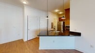 Located in Crozet, VA, this single-floor residence offers a thoughtfully designed open-concept layout that seamlessly connects the living, dining, and kitchen areas. The kitchen is a standout feature, boasting rich warm-toned wood cabinetry, dark granite countertops, and a full suite of stainless steel appliances, including a refrigerator, range, microwave, and dishwasher. A peninsula with a built-in sink and pendant lighting adds both functionality and style, making it an ideal space for cooking and entertaining. The living area is finished with rich hardwood-style flooring, crown molding, and a ceiling fan, while large windows and a glass-paneled exterior door flood the space with natural light and provide views of the surrounding neighborhood. A half-wall detail adds architectural interest and helps define the open floor plan. The bedroom features plush carpeting, a ceiling fan, and a generously sized window that brings in ample daylight. The bathroom is well-equipped with a soaking tub and shower combination, curved curtain rod, and brushed nickel fixtures and grab bars. The in-unit laundry area adds everyday convenience. Clean white walls and consistent finishes throughout contribute to a cohesive, move-in-ready aesthetic.