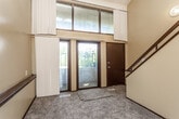 This two-floor split-level space offers a thoughtful layout with distinct living areas connected by a staircase. The entry level welcomes visitors through a glass-paneled front door framed by large transom windows, allowing generous natural light to pour into the carpeted foyer. A railed staircase leads to the upper and lower levels, creating a dynamic sense of vertical space.

The upper living area is highlighted by vaulted ceilings with an exposed beam, hardwood-style flooring, and a ceiling fan. An open railing overlooks the lower level, enhancing the airy, connected feel of the space. A second living or flex area on the upper floor features similar flooring, a vaulted ceiling, and windows with outdoor views.

The kitchen is well-appointed with warm oak cabinetry extending to the ceiling, granite-style countertops, a double sink, and white appliances including a range, refrigerator, and dishwasher. Light hardwood flooring adds warmth throughout.

Carpeted bedroom spaces offer a quieter retreat, with windows providing views of surrounding greenery. Two bathrooms serve the space — one featuring a full tub/shower combo with a white vanity, and another with a single vanity and toilet. Wood-style flooring runs through both bathrooms, maintaining a cohesive aesthetic throughout the home.