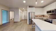 Located at The Birch on Washington Street in Conshohocken, PA, this single-floor residence offers a thoughtfully designed open-concept layout with modern finishes throughout. The kitchen serves as a focal point of the space, showcasing white upper cabinetry, two-tone gray lower cabinets, a textured tile backsplash, and a full suite of stainless steel appliances including a refrigerator, range, and microwave. A sleek white-topped island provides additional prep and dining space, with stylish pendant lighting overhead. Light wood-look flooring runs throughout the main living areas, lending warmth and visual continuity. The generously sized living area flows seamlessly from the kitchen, offering an open and airy atmosphere illuminated by recessed lighting. The bedroom features plush carpeting and a large window that brings in an abundance of natural light while offering exterior views. Two bathrooms are included: one with a large vanity, gray cabinetry, and wood-look flooring, and a second featuring a glass-enclosed walk-in shower and clean, neutral finishes. The overall design palette of soft neutrals, clean lines, and contemporary fixtures creates a bright, move-in-ready environment well-suited for modern living in the heart of Conshohocken.