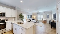 Located in Overland Park, Kansas, this well-appointed one-bedroom, one-bathroom residence offers a thoughtfully designed single-floor layout. The open-concept living room is bathed in natural light from large windows dressed with blinds and floor-to-ceiling drapes, complemented by a ceiling fan with a light fixture and light hardwood flooring that flows throughout the main areas. Crown molding adds a refined architectural touch to the living space.

The kitchen is a standout feature, boasting crisp white shaker cabinetry, quartz countertops with subtle veining, a full suite of stainless steel appliances, and a peninsula with bar seating — ideal for casual dining or entertaining. Recessed lighting keeps the space bright and functional.

The bedroom offers a comfortable retreat with plush carpeting, a ceiling fan, and a window that brings in natural light. It connects to a spacious walk-in closet with a full-width hanging rod and additional storage. A hallway leads to the clean, functional bathroom, which features a white vanity, storage cabinet, and light hardwood-style flooring. The layout is completed by a practical hallway connecting all areas cohesively, making efficient use of every square foot of this well-designed home.