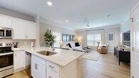 Located in Overland Park, Kansas, this well-appointed one-bedroom, one-bathroom residence offers a thoughtfully designed single-floor layout. The open-concept living room is bathed in natural light from large windows dressed with blinds and floor-to-ceiling drapes, complemented by a ceiling fan with a light fixture and light hardwood flooring that flows throughout the main areas. Crown molding adds a refined architectural touch to the living space.

The kitchen is a standout feature, boasting crisp white shaker cabinetry, quartz countertops with subtle veining, a full suite of stainless steel appliances, and a peninsula with bar seating — ideal for casual dining or entertaining. Recessed lighting keeps the space bright and functional.

The bedroom offers a comfortable retreat with plush carpeting, a ceiling fan, and a window that brings in natural light. It connects to a spacious walk-in closet with a full-width hanging rod and additional storage. A hallway leads to the clean, functional bathroom, which features a white vanity, storage cabinet, and light hardwood-style flooring. The layout is completed by a practical hallway connecting all areas cohesively, making efficient use of every square foot of this well-designed home.