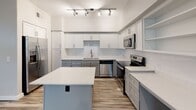 Located at 6500 Champion Grandview Way in Austin, Texas, this single-floor residence offers a well-designed layout that balances functionality and modern style throughout. The kitchen serves as a central highlight, outfitted with stainless steel appliances including a range, microwave, and dishwasher, complemented by two-tone cabinetry featuring white upper cabinets and gray lower cabinets, a white subway tile backsplash, and a central island with a clean white countertop. Track lighting illuminates the space, and wood-look plank flooring flows seamlessly throughout the unit. The open living area benefits from multiple windows that invite natural light and provide views of the surrounding greenery, while a ceiling fan with integrated lighting enhances comfort. Bedrooms are finished in neutral tones with wood-look flooring and feature built-in closet systems for organized storage. A dedicated laundry room houses a full-size washer and dryer alongside open shelving for added convenience. The bathroom is clean and functional, featuring a soaking tub and shower combination with white tile surround. Additional built-in shelving units in the hallway provide practical storage solutions, rounding out a thoughtfully designed living space.