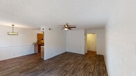 This single-floor residence offers a well-organized and functional layout that balances comfort with practicality. The living area is expansive and open, featuring rich dark hardwood-style flooring that extends throughout the space, crisp white walls, and a textured ceiling. A ceiling fan with a built-in light fixture anchors the room, while large sliding glass doors along one wall flood the space with natural light and provide direct access to an outdoor area. An open pass-through connects the living and dining areas to the kitchen, creating a seamless flow.

The galley-style kitchen is well-appointed with warm, medium-toned wood cabinetry lining both sides of the corridor, offering generous storage. Mosaic tile backsplashes add a decorative touch, and the countertops provide ample prep space. Black appliances, including a refrigerator and range, are neatly integrated into the cabinetry. Flush-mount ceiling lights illuminate the space efficiently.

The bedroom is a comfortable and quiet retreat, also featuring dark hardwood-style flooring, a ceiling fan with light, and a window fitted with vertical blinds that allow for natural light. A shiplap-style accent wall adds a subtle design element to the room. Throughout the residence, clean lines, neutral tones, and consistent flooring create a cohesive and inviting atmosphere.
