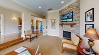 Located at 103 Melville Loop in Chapel Hill, NC, this single-floor community clubhouse offers a well-appointed and versatile gathering space designed to serve residents across a range of needs. The layout flows naturally between distinct functional areas, each finished with consistent warm-toned walls, crown molding, and recessed lighting throughout.

The kitchen is a standout feature, showcasing rich honey-toned cabinetry, granite countertops, a striking stacked-stone breakfast bar with pendant lighting, and a full suite of stainless steel appliances including a refrigerator, range, microwave, and dishwasher. The adjacent lounge area provides a comfortable retreat with plush seating, carpet flooring, and a dramatic floor-to-ceiling stacked-stone fireplace with a wood mantel and wall-mounted television. Natural light fills the space through large windows offering views of the surrounding greenery.

A dedicated business center features workstations and seating, while a quiet nook with a round table and chairs provides a more intimate setting for small gatherings or meetings. The fitness center is well-equipped with a treadmill, free weights, a weight bench, and a wall-length mirror, supported by natural light from multiple windows. Together, these spaces create a functional and welcoming community hub.