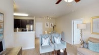 Beacon Place offers a thoughtfully designed single-story residence that maximizes its open-concept layout to create a comfortable and functional living environment. The living and dining areas flow seamlessly into one another, anchored by light hardwood-style flooring that extends throughout the space and contributes to a warm, cohesive aesthetic.

The living area is bright and airy, featuring a ceiling fan with a light fixture that provides both ventilation and ambient illumination. Neutral-toned walls enhance the sense of openness, while a doorway leads to additional private spaces within the unit. The dining area comfortably accommodates a small table and seating, making it well-suited for casual meals or entertaining.

The kitchen is positioned adjacent to the main living space and features dark cabinetry contrasted by light countertops, stainless steel appliances including a refrigerator, and a peninsula-style counter that subtly separates the cooking area from the dining space. Track lighting above the kitchen provides targeted task illumination. Overall, the unit presents a clean, modern, and inviting atmosphere suited for comfortable everyday living.