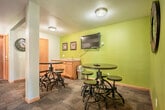 The Meadows Apartments amenity center is a compact, single-floor facility designed to serve residents with a range of fitness and productivity resources. A carpeted hallway connects the main areas, providing easy access throughout the space and contributing to a clean, organized layout with warm wood-trimmed doorframes and neutral-toned walls.

The fitness room is the centerpiece of the facility, featuring bold terracotta-orange accent walls that lend an energetic atmosphere. It is equipped with multiple treadmills, an elliptical trainer, a stationary bike, a dumbbell rack with a full wall mirror, an adjustable weight bench, and a folding exercise mat. A wall-mounted flat-screen television keeps residents entertained during workouts. Large sliding glass doors and windows flood the room with natural light and offer pleasant views of mature trees and green outdoor surroundings, enhancing the overall workout experience.

Adjacent to the fitness room, a separate mirrored area provides additional space for strength training and stretching. A posted exercise room rules sign ensures proper use and upkeep of the facility.

The business and lounge room offers a quiet, productive environment branded with The Meadows Apartments logo. It includes a built-in desk with computer workstations, task seating, and a round table with chairs for small meetings or collaborative work. A window provides natural light, and a wall-mounted air conditioning unit ensures year-round comfort.