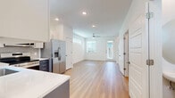 This two-story home in Hutto, Texas offers a well-designed layout across two floors, blending modern finishes with practical functionality. The main floor features an open-concept kitchen and living area with light hardwood flooring throughout. The kitchen is equipped with stainless steel appliances, including a French door refrigerator, gas range, built-in microwave, and dishwasher. Two-toned cabinetry — white upper cabinets paired with slate-blue lower cabinets — is complemented by a white quartz countertop and a classic subway tile backsplash. A ceiling fan and multiple windows allow natural light to fill the living area, creating a bright and airy atmosphere. A carpeted staircase leads to the upper floor, where the spacious primary bedroom features plush carpet, a ceiling fan, and multiple windows that invite natural light. The upper level also includes a well-appointed bathroom with a glass-enclosed tiled shower, a slate-blue vanity with white countertop, and wood-look flooring. A second bathroom is also present in the home. A dedicated closet and hallway provide additional storage and circulation. The home's clean, neutral palette and modern hardware selections give the entire space a cohesive and contemporary feel.