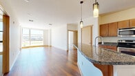 This thoughtfully designed 2-bedroom, 2-bathroom residence offers a functional and stylish single-floor layout. The open-concept living and kitchen area serves as the heart of the home, featuring rich hardwood flooring that extends throughout. The kitchen is equipped with stainless steel appliances, warm medium-toned wood cabinetry, and granite countertops that carry through to a peninsula with an integrated sink — ideal for casual dining or entertaining. Pendant lighting above the peninsula adds a refined touch.

The living area benefits from floor-to-ceiling windows that flood the space with natural light and offer open views of the surrounding outdoor environment. Both bedrooms are carpeted for comfort, with the primary bedroom providing a generous footprint and a walk-in closet. The secondary bedroom also features large windows that maximize daylight.

Each bathroom is finished with consistent granite vanity countertops, wood cabinetry, and clean tile flooring, complementing the overall design palette. A dedicated laundry area with a stacked washer and dryer unit adds everyday convenience. The cohesive use of granite, hardwood, and warm wood tones throughout creates a unified and welcoming ambiance across the entire residence.