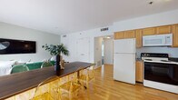 This single-floor residence offers a well-organized layout that balances open communal spaces with comfortable private retreats. The living room features light hardwood flooring, sage-green accent walls, and a large window that draws in natural light, creating an airy and inviting atmosphere. A wall-mounted television and ample floor space make it a functional gathering area.

The adjoining dining area flows naturally from the living space, anchored by a solid wood dining table paired with modern acrylic chairs. It connects directly to the kitchen, which is outfitted with light maple cabinetry, dark granite-style countertops, a full suite of white appliances including a refrigerator, electric range, microwave, and dishwasher, and hardwood-style flooring that continues the cohesive aesthetic.

The unit includes multiple bedrooms, each finished with plush carpeting. One bedroom features soft blue-gray walls and a large window, while another is distinguished by a rich sage-green accent wall and warm ambient lighting. A third bedroom offers a bright, neutral palette with ample natural light.

The bathroom is clean and functional, featuring full white-tile surround on the tub-shower combo and light tile flooring, lending a crisp, minimal finish to the space.