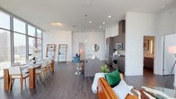 Located in the heart of downtown Los Angeles, this contemporary residence at 900 S Figueroa St offers a sleek, modern living experience defined by soaring floor-to-ceiling windows that frame breathtaking panoramic views of the city skyline. The open-concept layout seamlessly connects the living, dining, and kitchen areas, creating a bright and airy atmosphere bathed in natural light throughout the day. Dark hardwood-style flooring runs throughout, providing a refined contrast to the crisp white walls and high ceilings. The kitchen is thoughtfully designed with dark wood cabinetry, stainless steel appliances including a professional-grade range, a large center island with bar seating, and ample counter space. The living area features expansive glazed walls overlooking the Los Angeles skyline, while the dining space benefits from a dramatic floor-to-ceiling window wall offering unobstructed urban vistas. The bedrooms are generously proportioned, each with large windows capturing elevated city views. The bathrooms are finished in a clean, contemporary style, with one featuring a wide double vanity with a white countertop and illuminated mirror, and another offering a full soaking tub. This residence combines modern design with a prime downtown location for an elevated urban lifestyle.