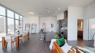 Located in the heart of downtown Los Angeles, this contemporary residence at 900 S Figueroa St offers a sleek, modern living experience defined by soaring floor-to-ceiling windows that frame breathtaking panoramic views of the city skyline. The open-concept layout seamlessly connects the living, dining, and kitchen areas, creating a bright and airy atmosphere bathed in natural light throughout the day. Dark hardwood-style flooring runs throughout, providing a refined contrast to the crisp white walls and high ceilings. The kitchen is thoughtfully designed with dark wood cabinetry, stainless steel appliances including a professional-grade range, a large center island with bar seating, and ample counter space. The living area features expansive glazed walls overlooking the Los Angeles skyline, while the dining space benefits from a dramatic floor-to-ceiling window wall offering unobstructed urban vistas. The bedrooms are generously proportioned, each with large windows capturing elevated city views. The bathrooms are finished in a clean, contemporary style, with one featuring a wide double vanity with a white countertop and illuminated mirror, and another offering a full soaking tub. This residence combines modern design with a prime downtown location for an elevated urban lifestyle.