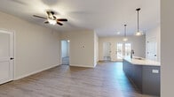 This single-story home features a thoughtfully designed open-concept layout that maximizes its comfortable footprint. The combined kitchen and living area forms the heart of the home, showcasing light gray luxury vinyl plank flooring, a ceiling fan, and French doors that invite natural light and outdoor views. The kitchen is a standout feature, equipped with gray shaker-style cabinetry, stainless steel appliances, subway tile backsplash, and a central island with a white countertop, undermount sink, and pendant lighting overhead.

The primary bedroom is a generously sized retreat with vinyl plank flooring, a ceiling fan, and an en-suite bathroom featuring gray vanity cabinetry, white countertops, a soaking tub, and access to a walk-in closet with wire shelving. The two additional bedrooms are carpeted, naturally lit by windows with blinds, and each equipped with ceiling fans. A dedicated closet with wood-tone vinyl plank flooring provides additional storage. Neutral warm-beige walls and clean white trim throughout the home create a cohesive, modern aesthetic.
