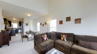 Summerfield Lofts offers a two-story layout designed to maximize space and comfort. The living area immediately impresses with its soaring vaulted ceilings, which create an airy, open atmosphere and lend the space a distinctly loft-like character. Large windows allow natural light to fill the room, brightening the neutral white walls and enhancing the overall sense of openness.

The main living space is generously proportioned, accommodating a full sectional seating area alongside a dedicated dining space, making it well-suited for both relaxing and entertaining. Soft wall-to-wall carpeting runs throughout the living and dining areas, adding warmth underfoot. The open flow between the living and dining zones creates a seamless and functional layout.

The kitchen is positioned adjacent to the main living area, providing convenient access without interrupting the open-plan design. The two-story configuration offers additional living or sleeping space on the upper level, taking full advantage of the vertical height established by the vaulted ceiling. Overall, the space combines a spacious, light-filled design with practical layout choices suited for everyday living.