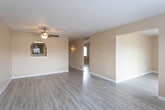 This single-story home presents a cohesive, functional layout with consistent design elements carried throughout. Light hardwood-style flooring runs across the living areas and bedrooms, complementing the warm beige tones of the walls and crisp white baseboards. Textured ceilings add visual character to the main living spaces, which are equipped with ceiling fans featuring built-in lighting fixtures for added comfort and practicality.

The living area is generously sized, receiving natural light through a large window, and connects to the kitchen via a charming arched pass-through opening — a distinctive architectural detail that enhances the sense of openness between the two spaces. A sliding glass door in one of the rooms provides access to the outdoors while allowing additional natural light to fill the interior.

The kitchen features white cabinetry, light countertops, a black gas range, and a subtle mosaic tile backsplash that adds texture to the cooking space. The bedrooms are well-proportioned with ample natural light from individual windows fitted with blinds. The bathroom includes a white vanity with cabinet storage, a mirrored medicine cabinet, wall-mounted lighting, and tiled accents, accessed conveniently from the hallway.