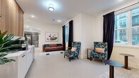 Located at 9821 Research Drive in Charlotte, NC, this well-appointed single-floor amenity space offers a thoughtfully designed layout across multiple functional areas. The two living room lounge areas are bright and welcoming, bathed in natural light streaming through large windows dressed with dramatic floor-to-ceiling black curtains. These spaces are furnished with a rich brown tufted leather sofa, vibrant floral-patterned wingback chairs, and a mix of round accent tables, all set atop textured area rugs against light, neutral-toned walls and smooth concrete-style flooring. Curated wall art adds a refined finishing touch to the relaxed, conversational atmosphere. The dedicated office area provides a more focused environment, seamlessly accessible from the main lounge. The standout feature of the space is the conference room, distinguished by a striking floor-to-ceiling black mural adorned with intricate white scrollwork and a prominent "Queen City" crown motif — a bold nod to Charlotte's nickname. A solid wood conference table surrounded by upholstered gray chairs sits beneath a modern globe chandelier, while a large window offers views of the surrounding neighborhood. Together, these spaces create a versatile, design-forward environment ideal for both collaboration and relaxation.