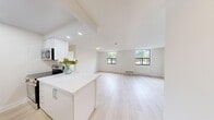 This well-designed 2-bedroom, 1-bathroom unit offers a clean, modern aesthetic with a thoughtful layout across a single floor. The open-concept living and kitchen area serves as the heart of the unit, featuring light wood-style flooring, crisp white walls, and recessed lighting that enhances the airy atmosphere. Large windows at the far end of the living room frame outdoor greenery views and allow abundant natural light to fill the space. The kitchen runs along one side in a galley configuration, outfitted with sleek white cabinetry, quartz countertops, stainless steel appliances including a microwave, electric range, and refrigerator, and light-toned flooring that flows seamlessly into the main living area. Both bedrooms are generously proportioned, bright, and finished with the same light flooring, each featuring windows with outdoor views and baseboard heating. The primary bedroom offers a comfortable footprint well-suited for a full furniture arrangement. Two closets provide ample storage throughout the unit. The full bathroom is finished in a clean, minimalist style with a white vanity, integrated sink, mirror, and a tub-shower combination. A dedicated laundry area and hallway complete the functional layout of this well-appointed unit.