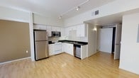 Located at 1801 L St, this single-floor space offers a clean, modern aesthetic with an open-concept design that maximizes the sense of space and flow. The kitchen is a standout feature, outfitted with crisp white cabinetry, dark countertops, and a suite of stainless steel appliances including a full-size refrigerator, built-in microwave, dishwasher, and a white range. Track lighting runs along the ceiling, providing versatile and adjustable illumination throughout the space. The light hardwood flooring extends seamlessly from the kitchen into the open living area, creating a cohesive and inviting atmosphere. Ceilings are elevated, enhancing the airy, open feel of the interior. The layout transitions naturally from the kitchen toward a separate room area, offering functional separation while maintaining an overall sense of openness. Neutral wall tones keep the space bright and adaptable to a variety of uses. Ventilation is provided via ceiling vents, ensuring year-round comfort. The overall ambiance is contemporary, clean, and highly functional, making it a practical and welcoming space at 1801 L St.
