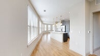 Located at 612 N Zang Blvd in Dallas, TX, this well-appointed 2-bedroom, 2-bathroom residence offers a thoughtfully designed single-floor layout with a distinctive architectural character. The standout feature is the curved living room, where a sweeping arc of windows floods the space with natural light and city views, complemented by light hardwood flooring and a ceiling fan overhead.

The open-concept kitchen flows seamlessly from the living area and is appointed with two-tone cabinetry — cool gray lowers paired with crisp white uppers — alongside stainless steel appliances, a white quartz island, subway tile backsplash, and elegant gold pendant lighting. This kitchen is as functional as it is visually striking.

Both bedrooms are carpeted for comfort, each featuring ceiling fans and multiple windows with city-facing views. The primary bedroom offers generous proportions, while both rooms provide access to dedicated closets.

The bathrooms are finished with a cohesive design palette: classic white subway tile surrounds the soaking tub, hexagonal mosaic tile floors add texture underfoot, and sleek gray vanities with brass fixtures lend a refined, modern touch. A hallway connects the spaces efficiently, adding to the unit's practical flow.

Overall, the residence presents a clean, contemporary aesthetic with warm metallic accents throughout.