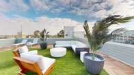 Located at 1801 Main St in Columbia, South Carolina, this rooftop terrace offers a well-appointed outdoor retreat above the downtown cityscape. The space is thoughtfully designed, combining two distinct surface materials — warm-toned interlocking wood deck tiles and vibrant artificial turf — to create defined zones for relaxing and dining.

The lounge area features a contemporary sectional sofa with light upholstery, complemented by a sculptural white round coffee table and a teak-framed armchair with plush white cushions. Large decorative planters with tropical palms are positioned throughout, adding lush greenery and a resort-like atmosphere. A separate dining nook, set on the wood-tiled deck near the glass entry doors, includes a round table and coordinating chairs, ideal for casual meetings or al fresco meals.

The perimeter is enclosed by a soft sage-green low wall with glass panel accents, maintaining open sightlines to the surrounding Columbia skyline, including notable high-rise buildings and local landmarks visible from multiple vantage points. Sun loungers are also available along the deck's edge.

The open-air layout and abundance of natural light make this rooftop terrace a versatile space suited for gatherings, events, or everyday outdoor enjoyment in an urban setting.
