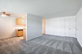 Located at 500 Peconic St in Ronkonkoma, New York, this single-floor unit offers a practical and well-organized layout designed for comfortable everyday living. The spacious living area is finished with plush wall-to-wall carpeting and neutral-toned walls, creating a clean and inviting atmosphere. Natural light filters in through a multi-pane window adjacent to the front entry door, which also features a wall-mounted HVAC unit and baseboard heating for year-round climate control. A half-wall partition separates the living area from the kitchen, maintaining an open feel while defining each space. The galley-style kitchen is outfitted with warm oak cabinetry, light-toned countertops, and a full suite of stainless steel appliances including a gas range, dishwasher, microwave, and refrigerator. Tile flooring runs throughout the kitchen, complementing the cabinetry tones. Interior doors lead to additional rooms, including a closeted bedroom area visible in the floor plan. The bathroom features a white vanity with an integrated sink, a mirrored medicine cabinet offering storage, and a clean, minimalist finish throughout. Overall, the unit presents a functional and move-in-ready space in a convenient Long Island location.
