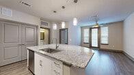 Located at 14900 Memorial Dr in Houston, Texas, this one-bedroom, one-bathroom residence offers a well-designed single-floor layout that maximizes functionality and style. The open-concept kitchen and living area serves as the heart of the home, anchored by a striking curved island with granite countertops and a stainless steel sink, illuminated by elegant pendant lighting. The kitchen is fully equipped with stainless steel appliances, including a French door refrigerator, electric range, microwave, and dishwasher, complemented by white cabinetry with ample storage and a mosaic tile backsplash. Dark hardwood-style flooring extends throughout the main living area, adding warmth and visual continuity. The living room benefits from natural light streaming through large windows fitted with blinds, and a ceiling fan enhances comfort. A private balcony offers additional outdoor space. The carpeted bedroom is a comfortable retreat, featuring a ceiling fan, a large window with natural light, and direct access to two closets, including a walk-in with built-in shelving. The bathroom is finished with granite countertops, white cabinetry, a large framed mirror, and tile flooring. An in-unit laundry area adds everyday convenience to this thoughtfully appointed Houston residence.